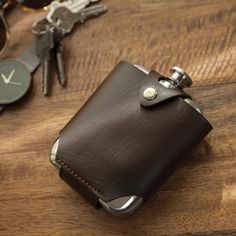 a brown leather flask with keys on a wooden table next to glasses and watch