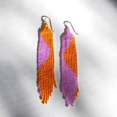 two pairs of beaded earrings with orange and purple designs on them sitting on a white surface