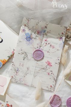 some cards and buttons are laying on a table with flowers, feathers and other items