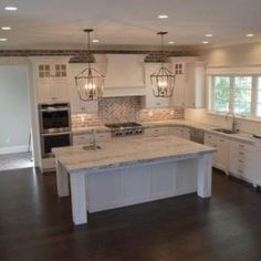 a large kitchen with white cabinets and an island in the middle of the room is lit by two pendant lights