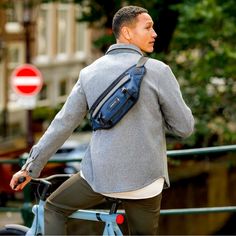 a man riding a bike with a blue bag on it's back and his hand in his pocket