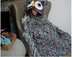 a woman sitting in a chair with a crocheted owl blanket over her head