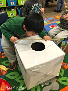 a young boy is playing with an object in the classroom while another child looks on