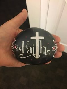 a hand holding a painted rock with the word faith on it and a cross in the middle