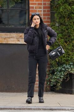 a woman is talking on her cell phone while walking down the street with a handbag