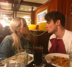 a man and woman sitting at a table eating spaghetti