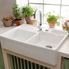 a white kitchen sink sitting on top of a counter next to potted planters