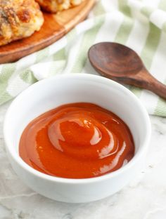 a white bowl filled with sauce sitting on top of a table next to some bread