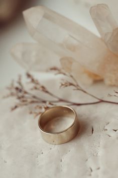 two gold wedding rings sitting on top of a table next to some crystal rocks and flowers