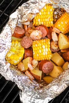 corn on the cob with sausage, potatoes and shrimp in foil wrapper over charcoal grill