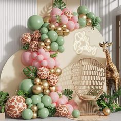 a giraffe standing next to a wall with balloons and greenery on it