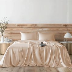 a bed with beige sheets and pillows in a white room next to a wooden headboard