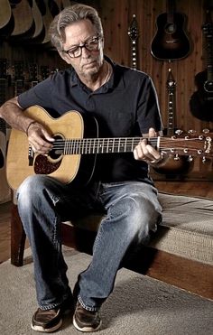 a man sitting on top of a bed holding a guitar in his hand and playing the guitar