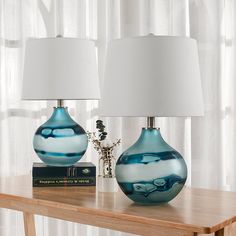 two blue glass vases sitting on top of a wooden table next to a lamp