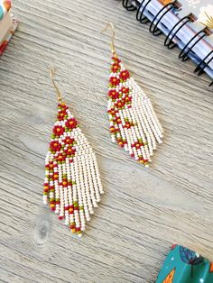 a pair of white and red beaded earrings sitting on top of a wooden table