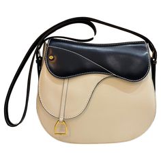 This beautiful vintage GUCCI two-toned saddle bag is crafted of smooth calfskin leather in off-white and navy featuring gold toned hardware. Front magnetic snap closure decorated with a stirrup charm opens to a beige leather interior with a zippered pocket. A very rare quiet luxury piece from The House of Gucci. Made in Italy. Measures approximately 9 x 8.5 x 3 inches Strap drop 20 inches at its longest. Comes with dust bag. Condition - Very good vintage condition with minor signs of wear Outsid Vintage Gucci Bag, Cream Purse, Gucci Vintage Bag, Shoulder Bag Vintage, Gucci Outfits, Gucci Monogram, Gucci Shoulder Bag, Black Leather Crossbody Bag, Gucci Leather