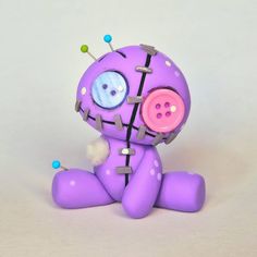 a purple stuffed animal with buttons on it's face and legs sitting down in front of a white background