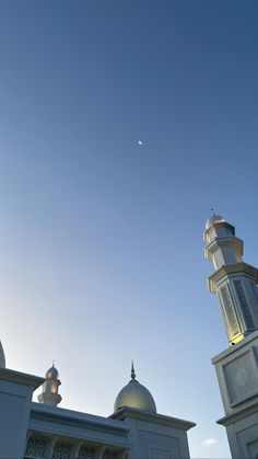 a tall white building with two domes on top and a moon in the sky above it