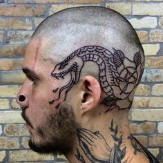 a man with a dragon tattoo on his head and behind his ear is a brick wall