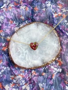 a strawberry necklace sitting on top of a white piece of rock next to a purple flowered cloth