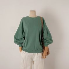 a mannequin wearing a green sweater and white pants, holding a brown purse