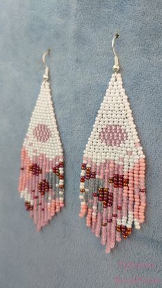 two pink and white beaded earrings hanging from hooks on a blue cloth covered surface