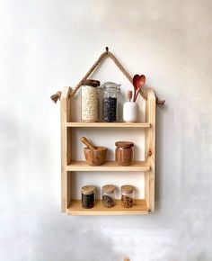 a wooden shelf with jars and spoons hanging from it's sides on a wall