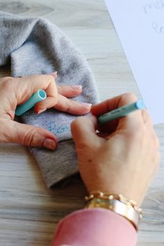 a woman's hands holding a pen and writing on a piece of paper next to a pair of scissors