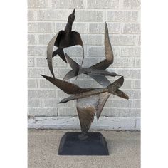 three metal birds on a black base in front of a white brick wall and cement floor