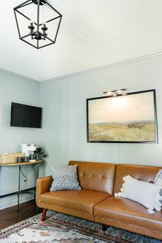 a living room with a brown leather couch and tv mounted on the wall above it