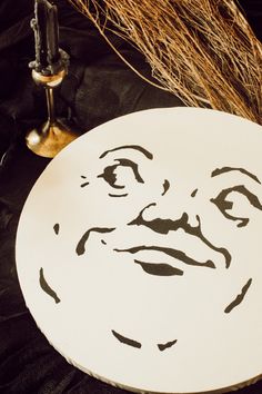 a white plate with a face drawn on it next to a candle and some dry grass