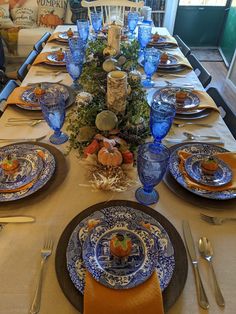 the table is set with blue and white plates, silverware, and pumpkins