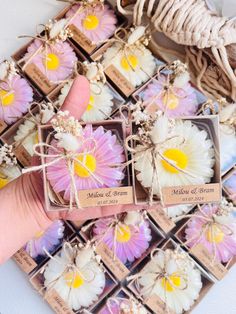 hand holding small boxes filled with flowers on top of a white table next to string