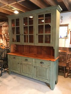 an old green china cabinet with glass doors and wooden top in a room full of chairs