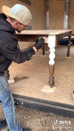 a man is painting a table with white paint and black gloves on his hands while he stands in front of the table