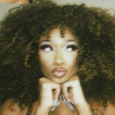 a woman with large curly hair posing for a photo in front of a mirror and holding her hands on her chest