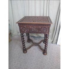 an old wooden table with carvings on the top and legs, sitting in front of a curtain