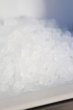 a pile of ice sitting on top of a metal counter next to a bowl filled with water