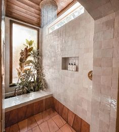 a bathroom with tiled walls and flooring next to a window, shower head and plants