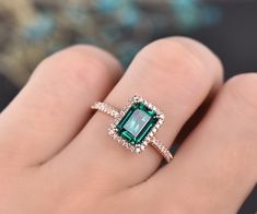 a woman's hand holding an emerald and diamond ring