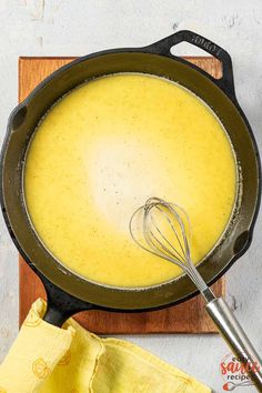 a frying pan filled with yellow liquid next to a whisk on a cutting board