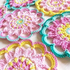 crocheted flowers are arranged in rows on a white tablecloth with yellow, pink, and blue trim