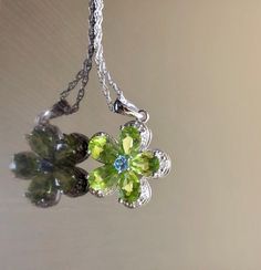 DeKara Designs Silver Metal- Sterling Silver, .925. Stones- 5 Natural Pear Shape Peridot 5 Carats, 1 Round Natural Blue Topaz, 5 Diamonds G-H Color SI2 Clarity 0.02 Carats. Measurements- Necklace is 18 Inches Long. Pendant is Bit Over An Inch Long Including Bail. Beautifully handmade Art Deco inspired halo diamond blue topaz peridot necklace made in sterling silver. There are five natural beautiful green pear shape peridot stones that are all professionally prong set. There is a prong set round Fine Jewelry Peridot Necklace For May Birthstone, Green Multi-stone Round Necklace, Green Round Necklace With Gemstone Accents, Green Multi-stone Round Necklaces, Green Round Necklaces With Gemstone Accents, Fine Jewelry Peridot Necklace For Anniversary, Lime Green Peridot Jewelry For May Birthstone, Green Peridot Gemstone Necklace, Green Gemstone Flower Pendant Jewelry