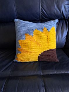 a crocheted sunflower pillow on a black leather couch with blue and yellow pillows