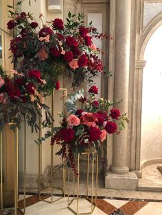 two tall gold vases with red flowers and greenery