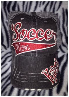 a baseball cap with the word soccer mom on it in red and white letters, sitting on a zebra print background