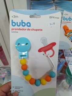 a hand holding a blue and orange pacifier in front of some other baby products