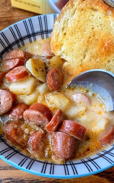 there is a bowl of soup with sausage and bread on the table next to it