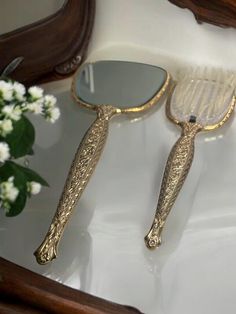 two gold colored hair brushes sitting on top of a white sink next to a mirror