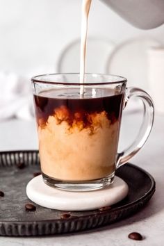 coffee being poured into a glass cup on top of a black tray with chocolate chips